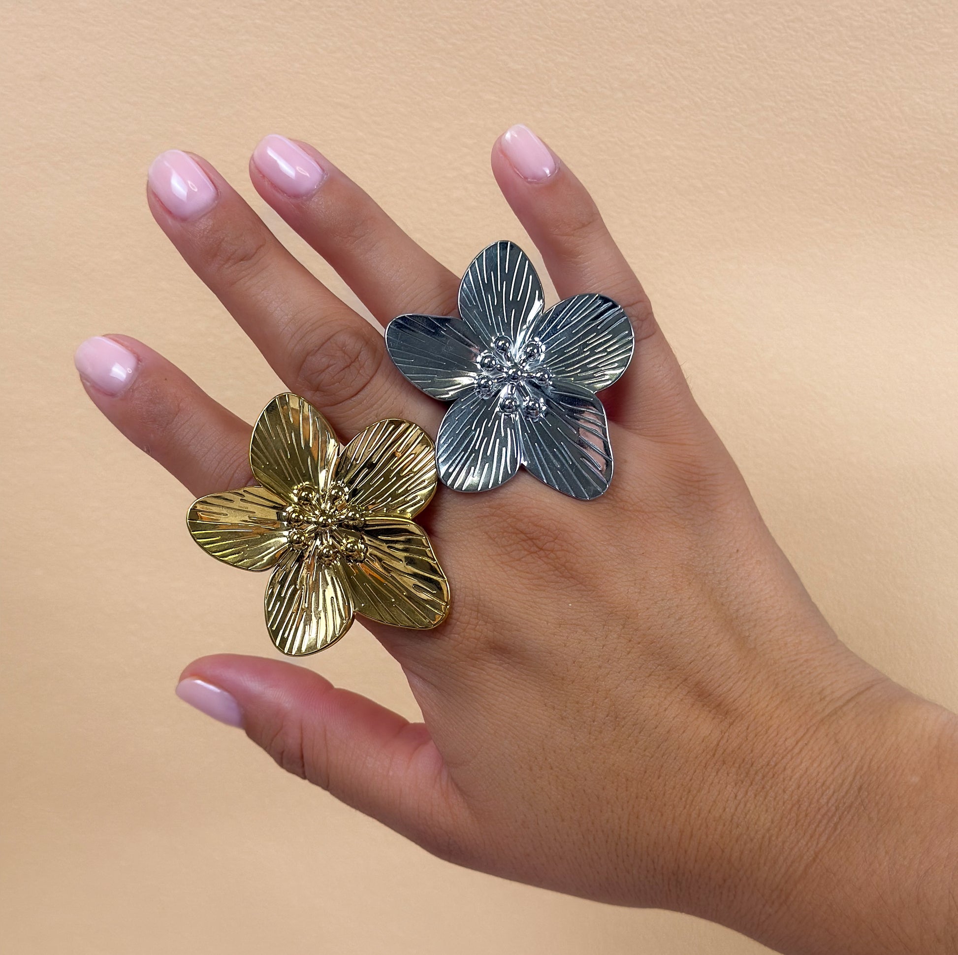 Gold and silver flower-shaped rings on a hand against a beige background