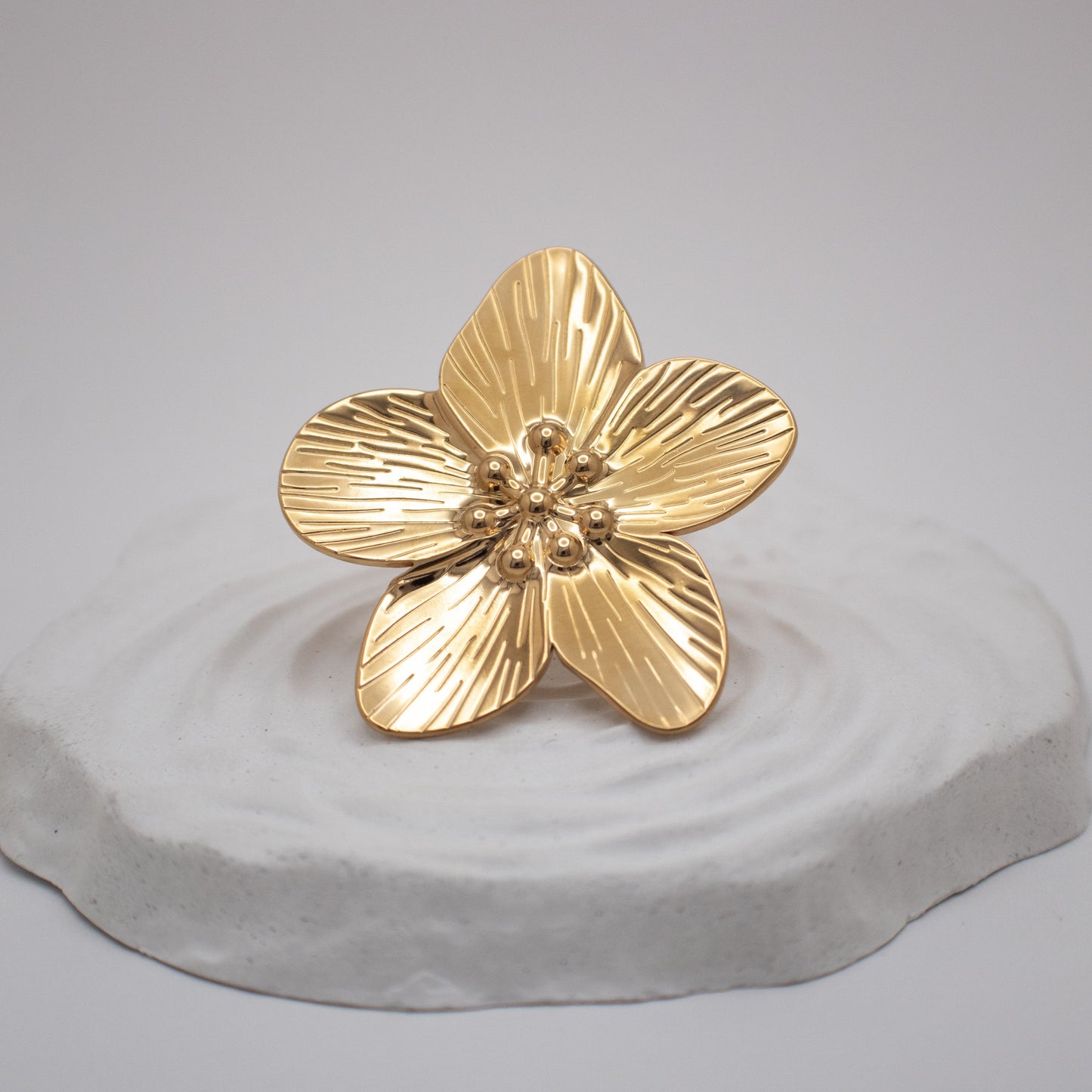 Gold flower-shaped object on a gray pedestal against a light gray background