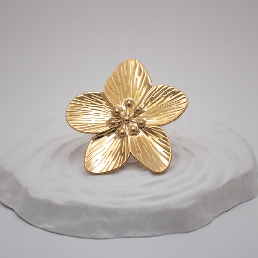 Gold flower-shaped object on a gray pedestal against a light gray background