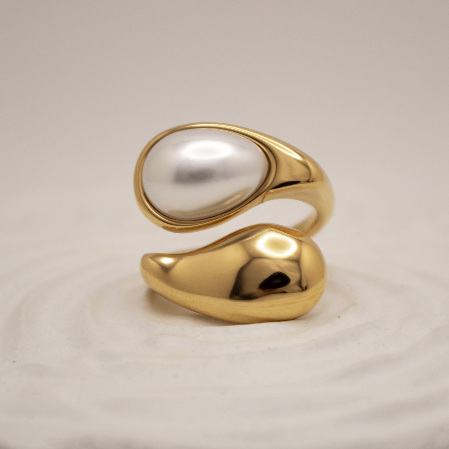 Gold ring with a central pearl on a beige background
