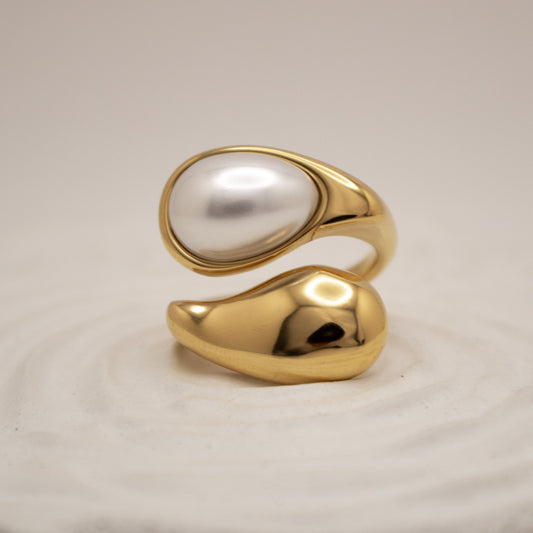 Gold ring with a central pearl on a beige background