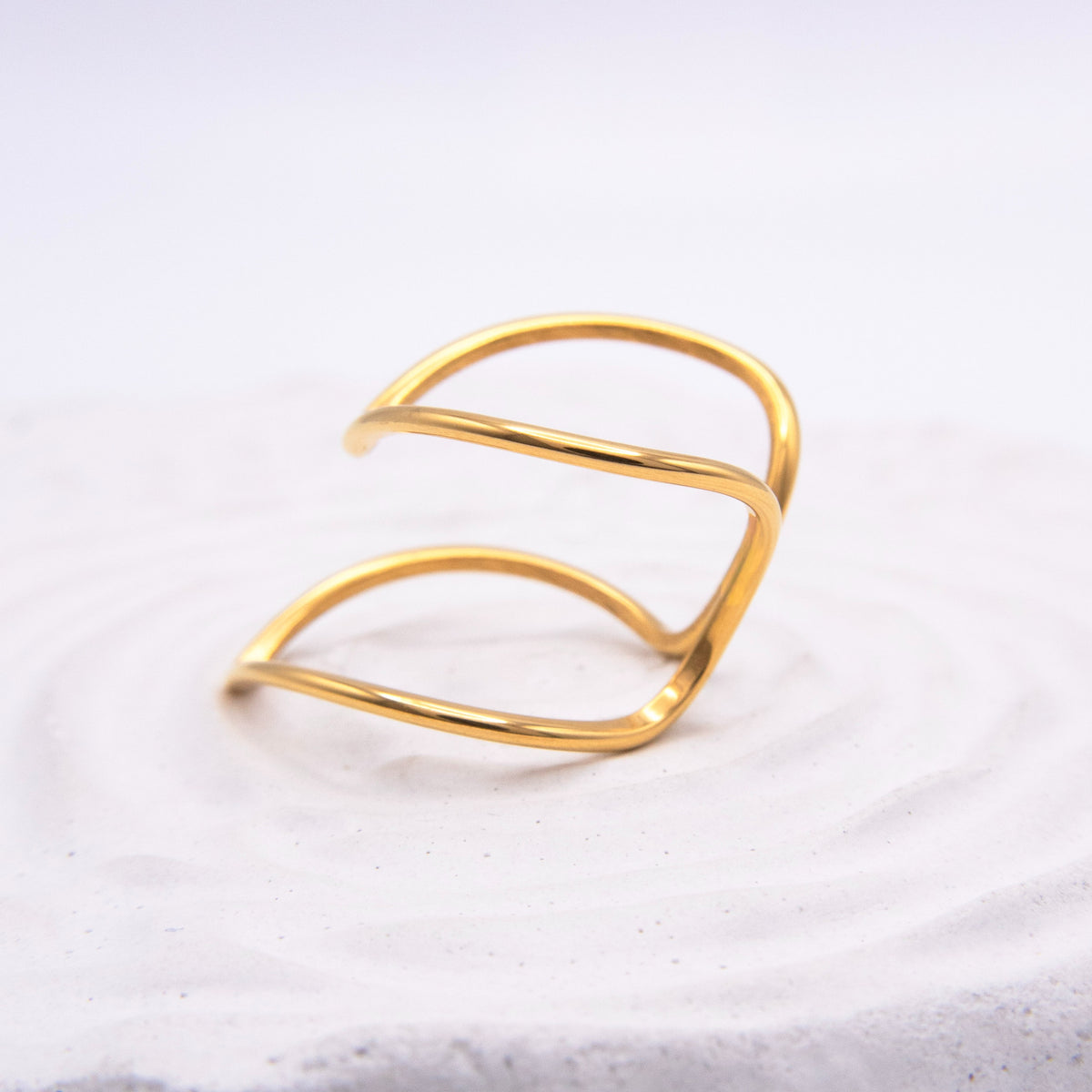 Open sculptural gold ring with flowing curved lines.