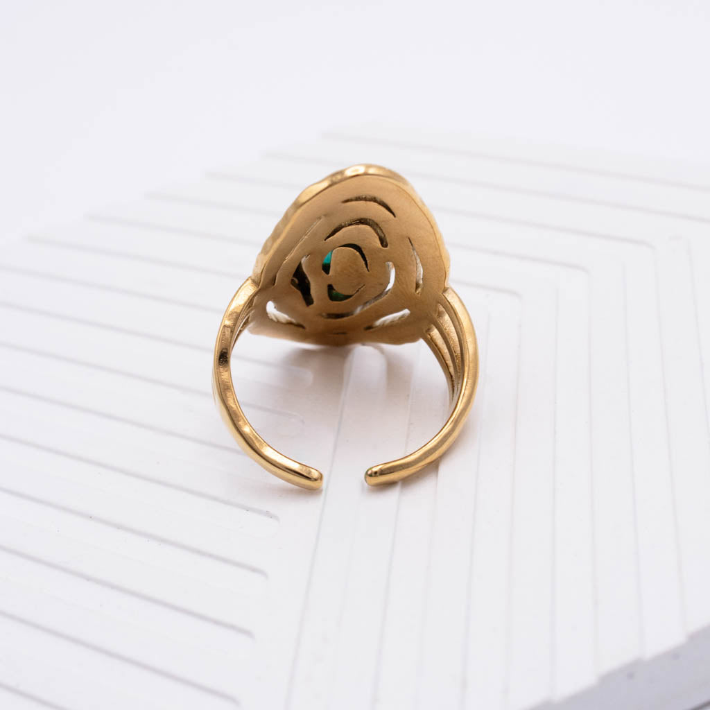 A gold-toned adjustable ring with a sculptural, openwork floral or spiral design on the top, resting on a white textured surface.