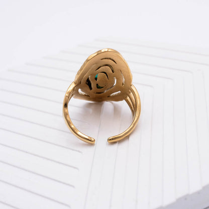 A gold-toned adjustable ring with a sculptural, openwork floral or spiral design on the top, resting on a white textured surface.
