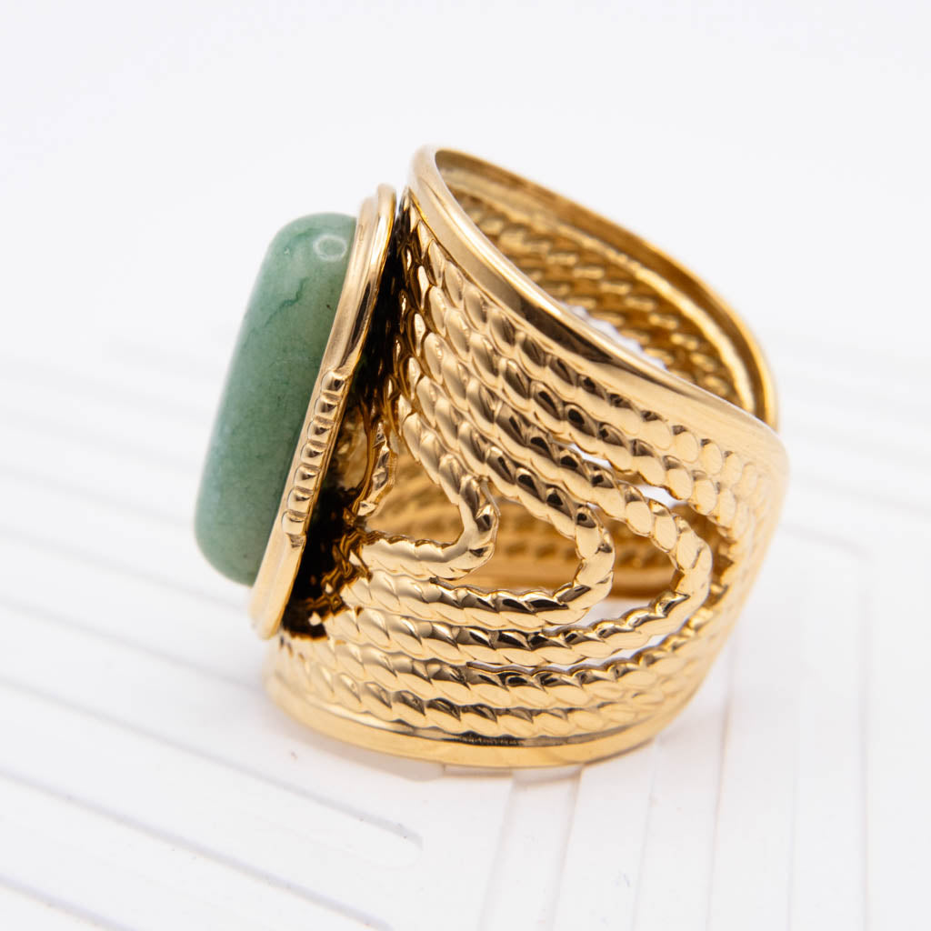 A wide gold ring with a textured, snake-like hammered band and a smooth green stone inset on the side, photographed on a white background.