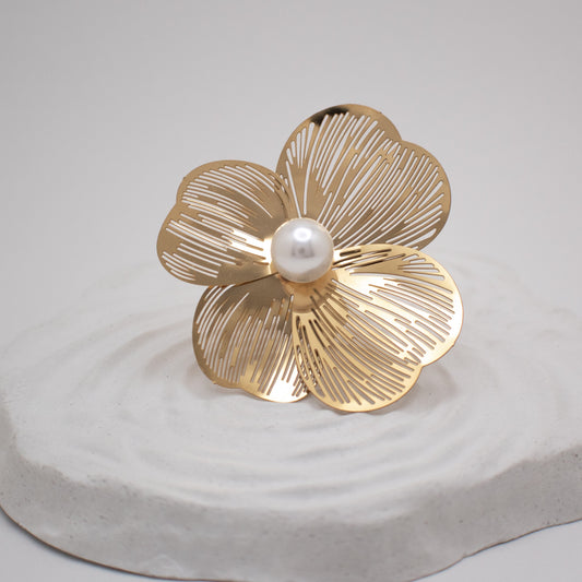 Gold flower-shaped brooch with a pearl center on a light gray background