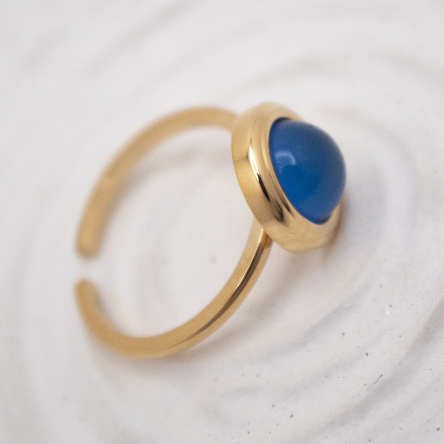 Gold ring with a blue gemstone on a light gray background