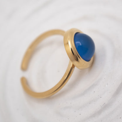Gold ring with a blue gemstone on a light gray background