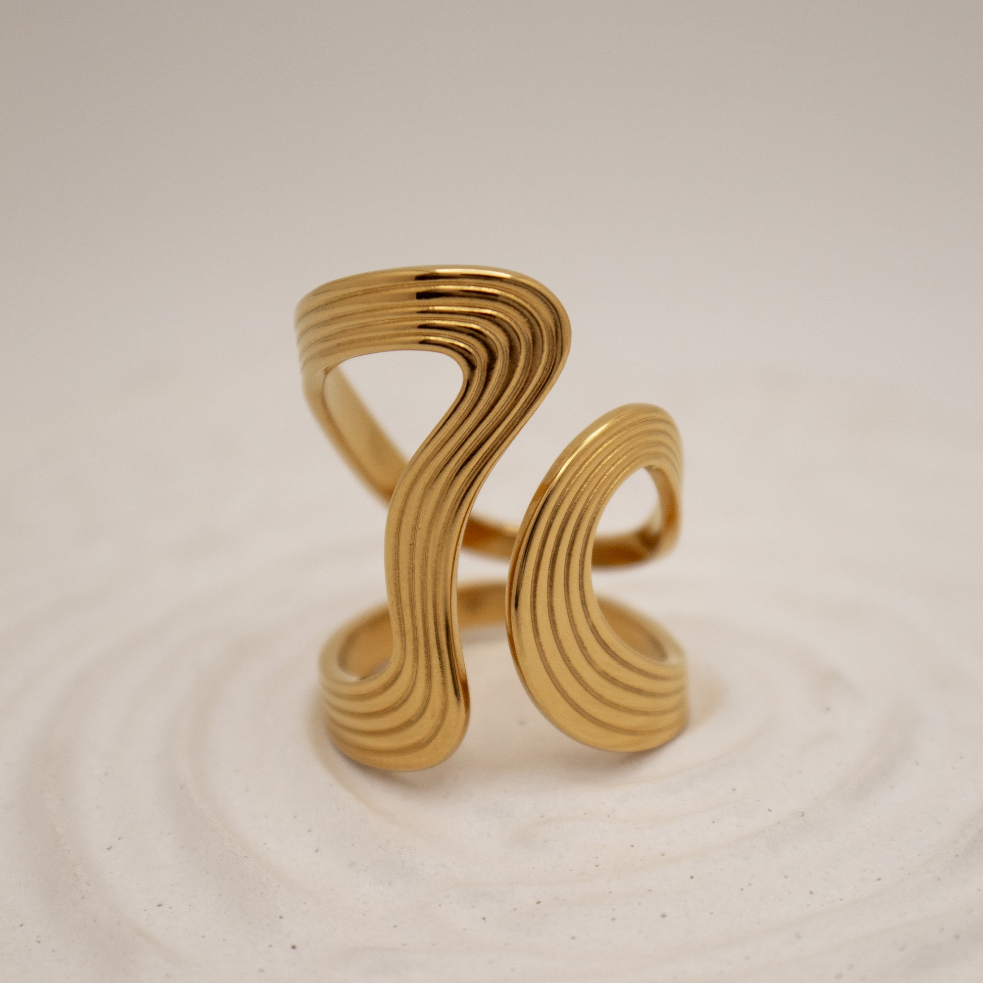 Gold ring with wavy design on a beige background