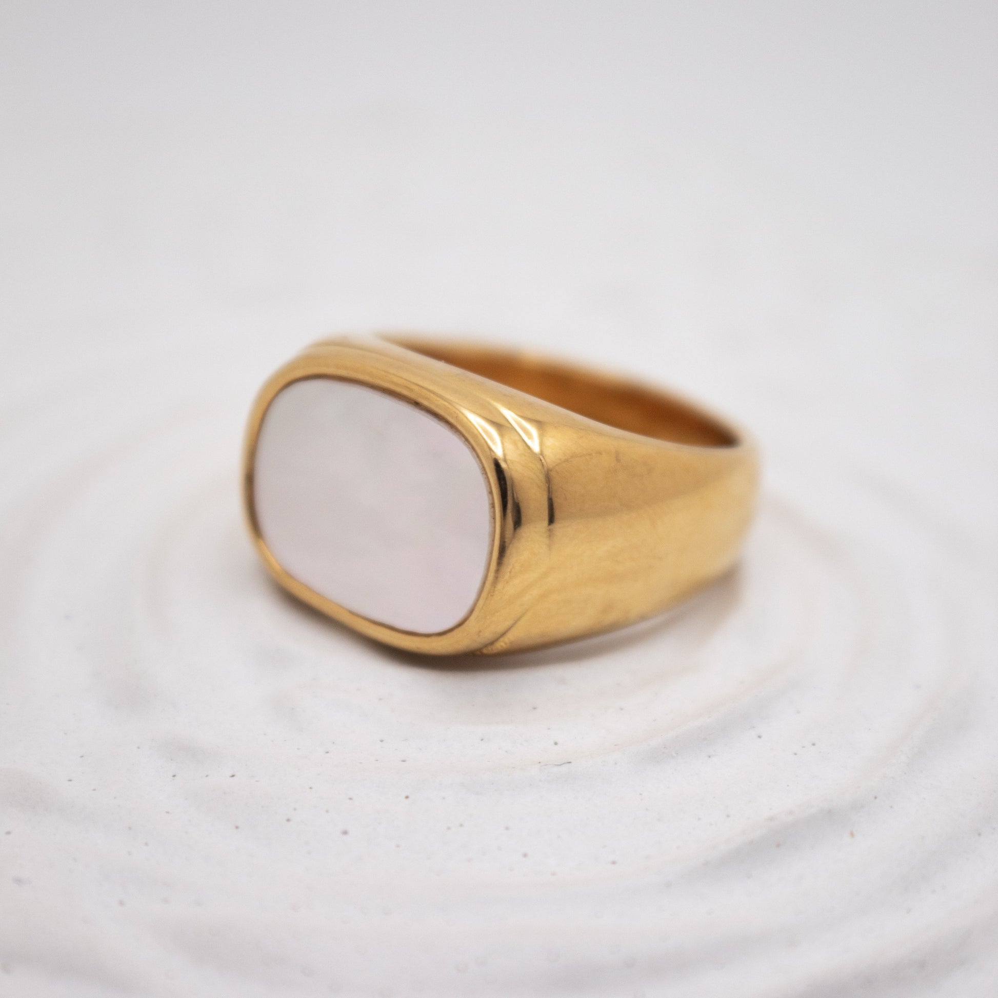 Gold ring with a white stone on a textured white background