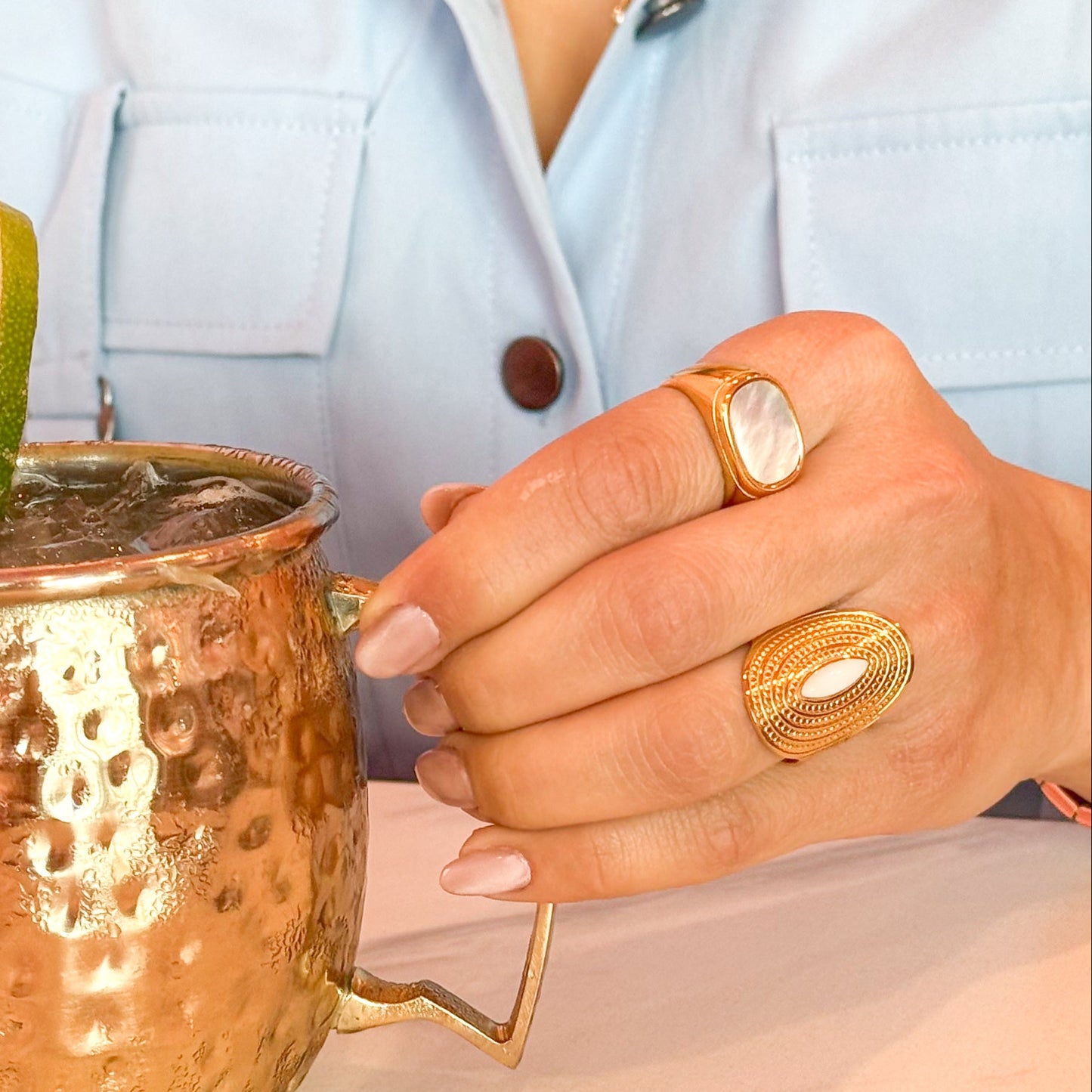 Person holding a copper mug with a lime wedge, wearing gold jewelry.