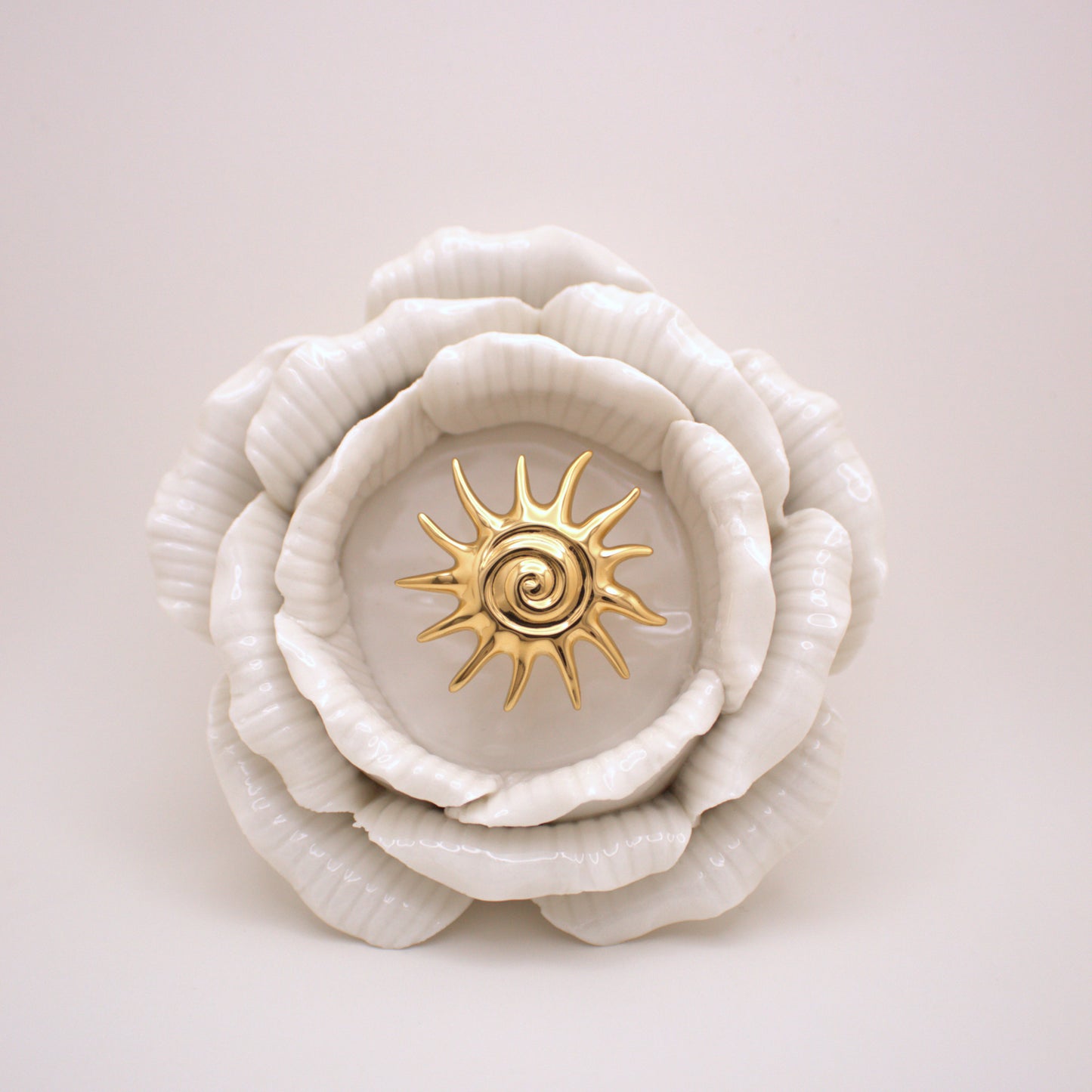 White ceramic flower with a gold center on a light pink background