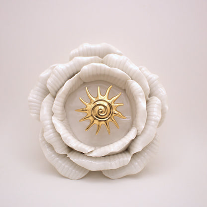 White ceramic flower with a gold center on a light pink background