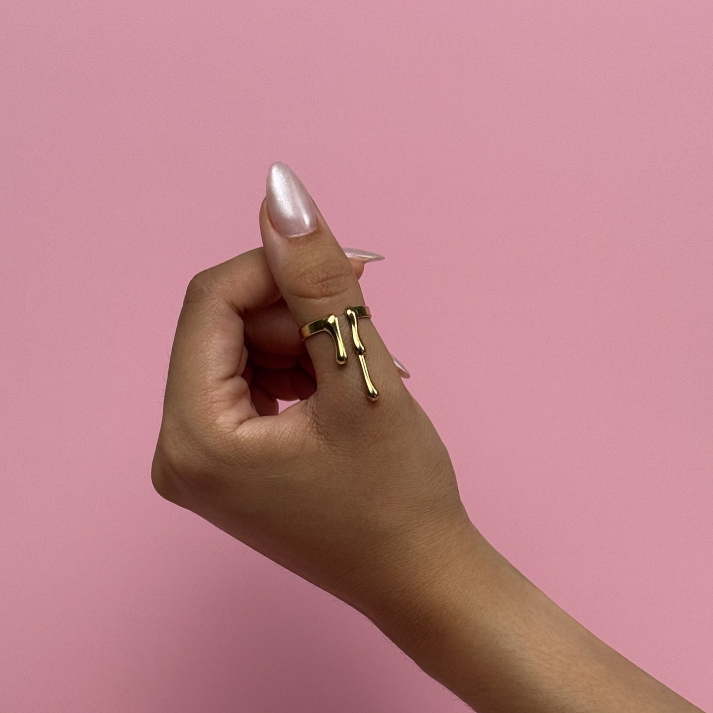 Hand holding a gold ring against a pink background