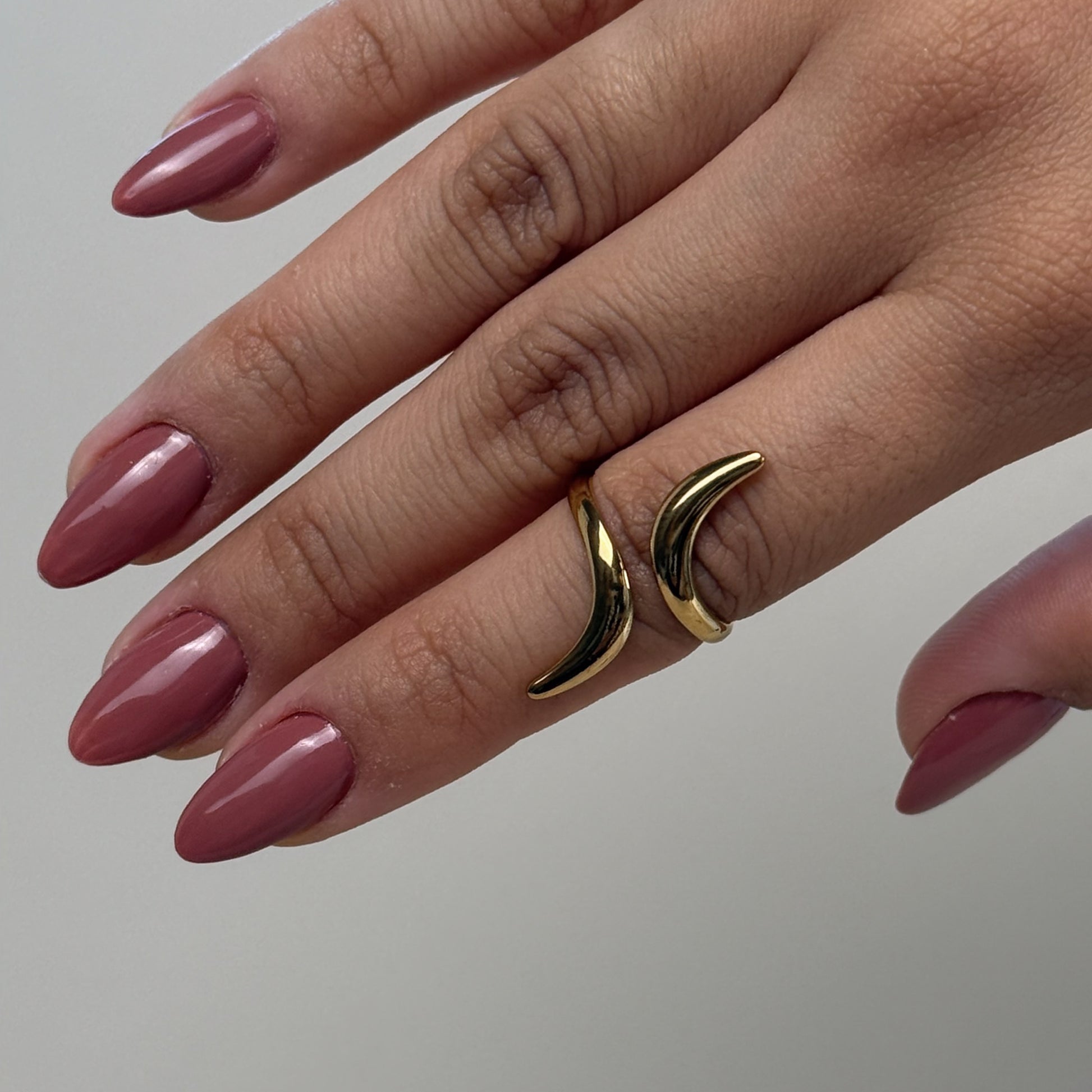Hand wearing two gold rings with a plain background