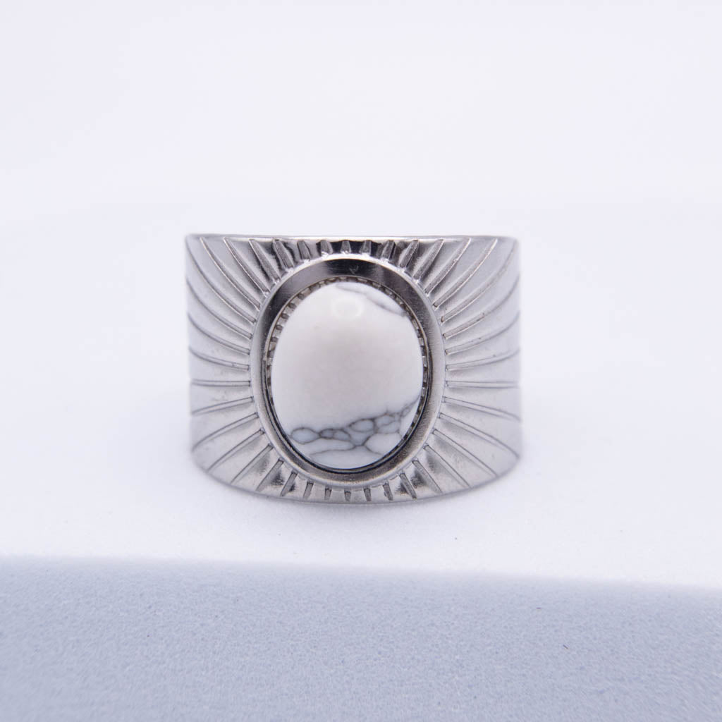 A wide silver-toned ring with a textured sunburst design and a central oval cabochon featuring a white and gray marbled pattern, set against a clean white background.