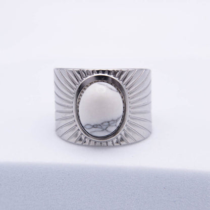 A wide silver-toned ring with a textured sunburst design and a central oval cabochon featuring a white and gray marbled pattern, set against a clean white background.