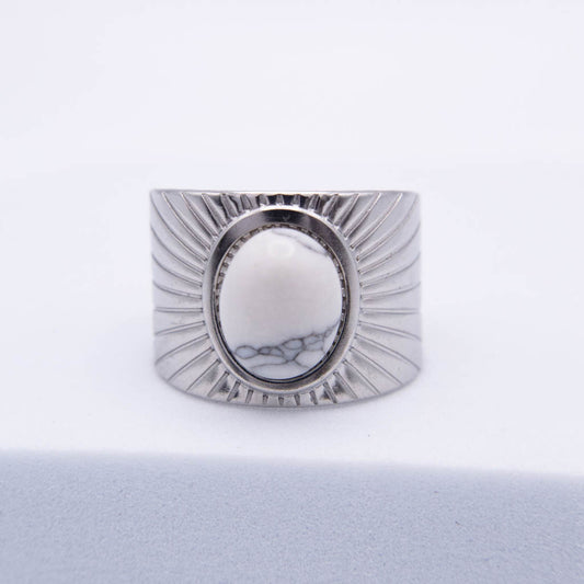 A wide silver-toned ring with a textured sunburst design and a central oval cabochon featuring a white and gray marbled pattern, set against a clean white background.