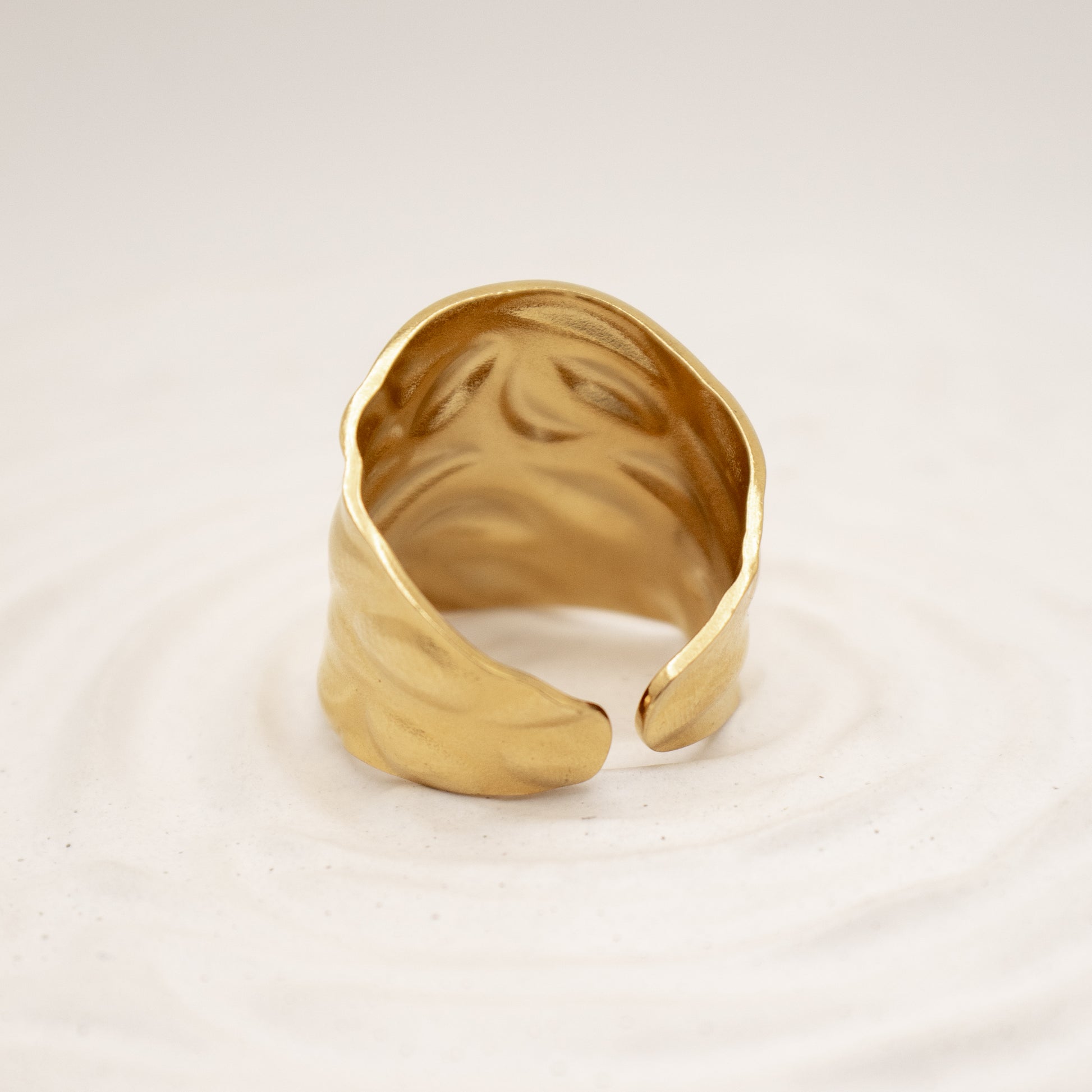 Gold ring with wavy design on a light beige background