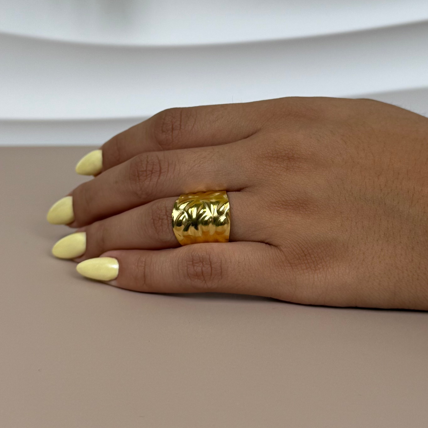 Hand wearing a gold ring with a neutral background