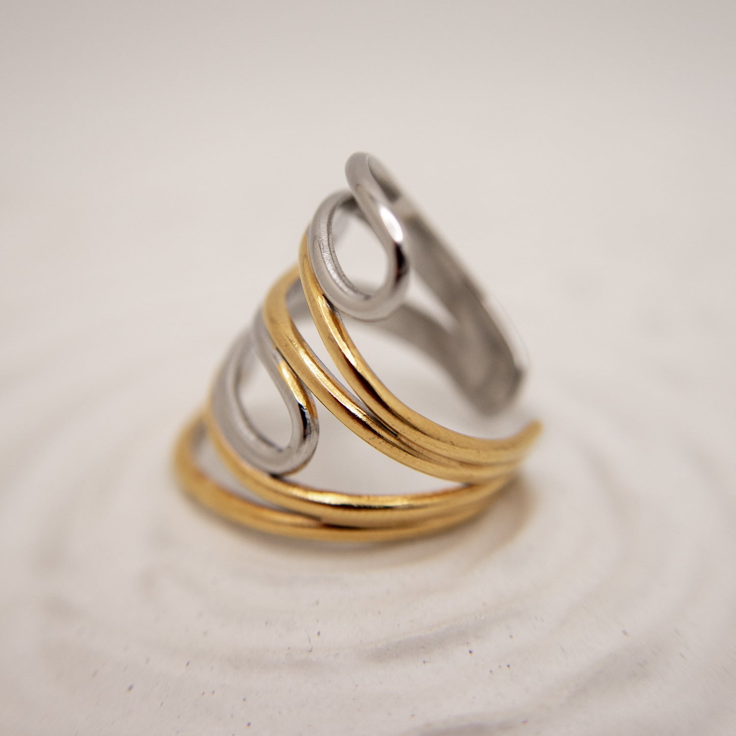 Three metallic rings in gold, silver, and bronze on a light beige background