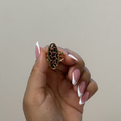 Hand holding a gold ring with a leopard print design against a neutral background