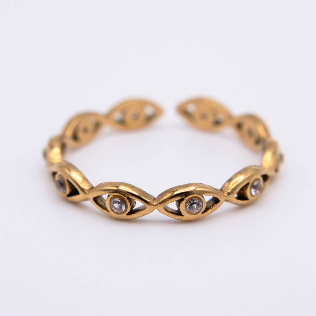A gold cuff bracelet featuring a series of stylized eye motifs, each detailed with small clear gemstones, set against a plain white background.