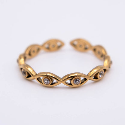 A gold cuff bracelet featuring a series of stylized eye motifs, each detailed with small clear gemstones, set against a plain white background.
