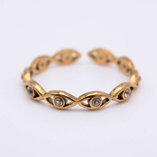 A gold cuff bracelet featuring a series of stylized eye motifs, each detailed with small clear gemstones, set against a plain white background.