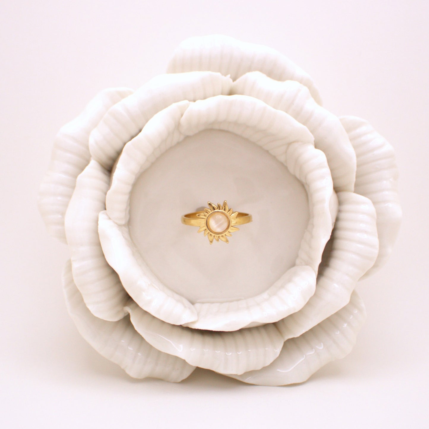 White ceramic flower-shaped dish with a gold ring on a light pink background