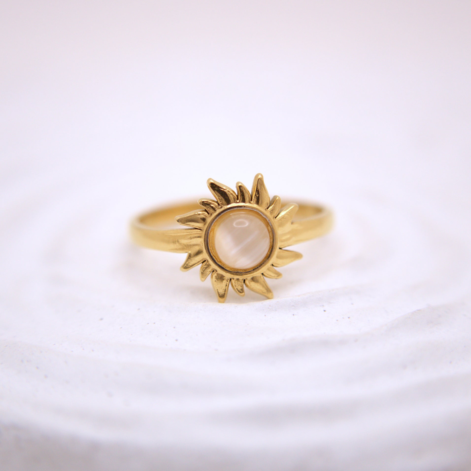 Gold sun-shaped ring with a central stone on a white background