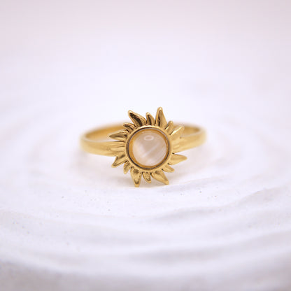 Gold sun-shaped ring with a central stone on a white background
