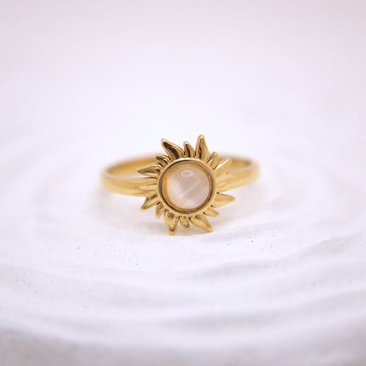 Gold sun-shaped ring with a central stone on a white background