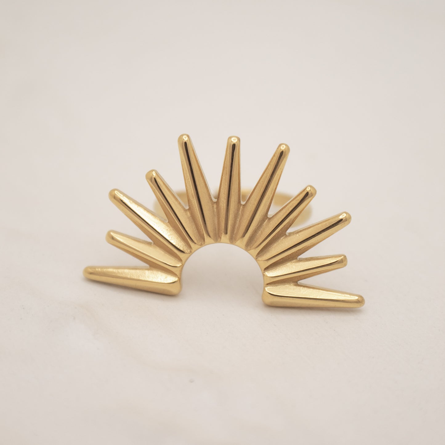 Gold sunburst ring on a beige background