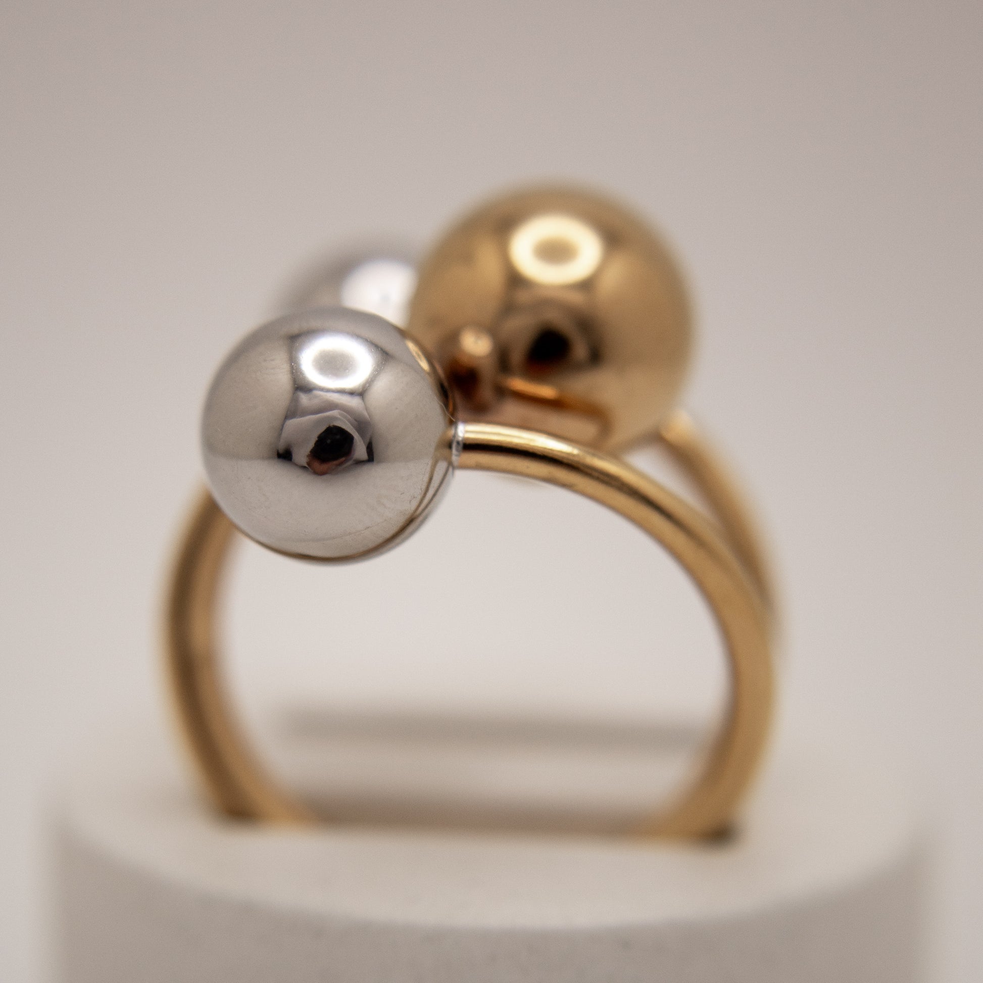 Two gold rings with spherical ends on a light gray background