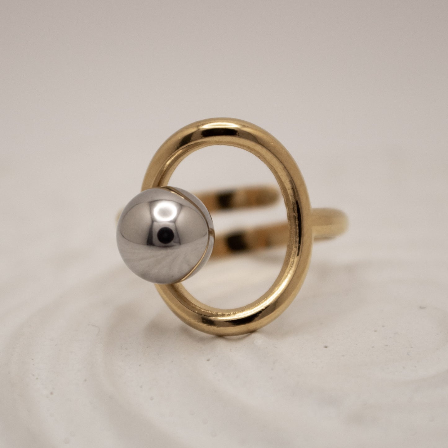 Gold ring with a silver sphere on a light gray background