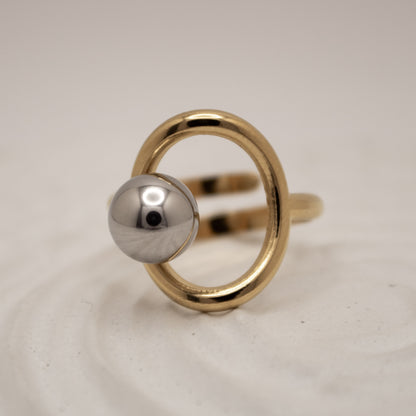 Gold ring with a silver sphere on a light gray background