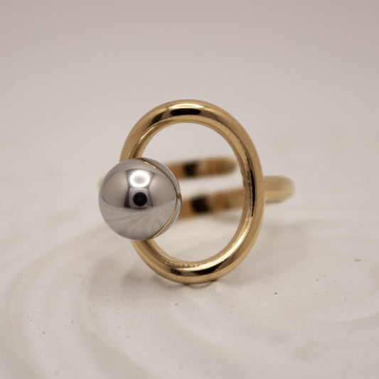 Gold ring with a silver sphere on a light gray background