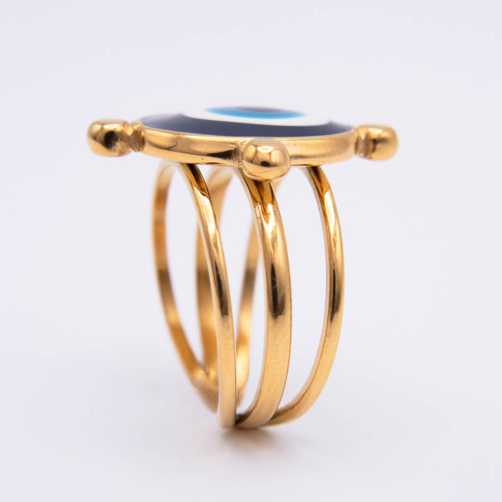 A gold-plated evil eye ring with a multi-band design and a round evil eye stone on top, set against a plain white background.
