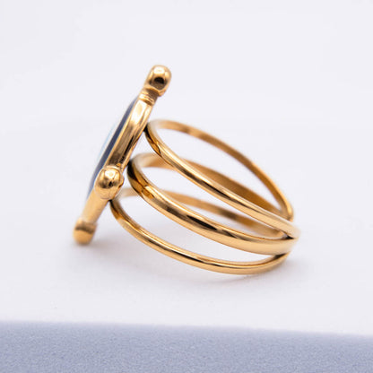 A gold-plated multi-band ring with a round bezel-set dark blue stone, shown from a side profile on a white background.