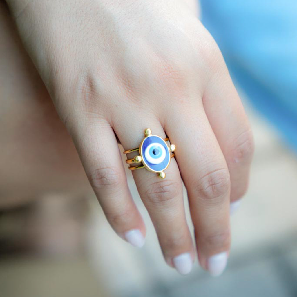 A gold ring featuring an evil eye design with blue, white, and black concentric circles, worn on a person's finger.