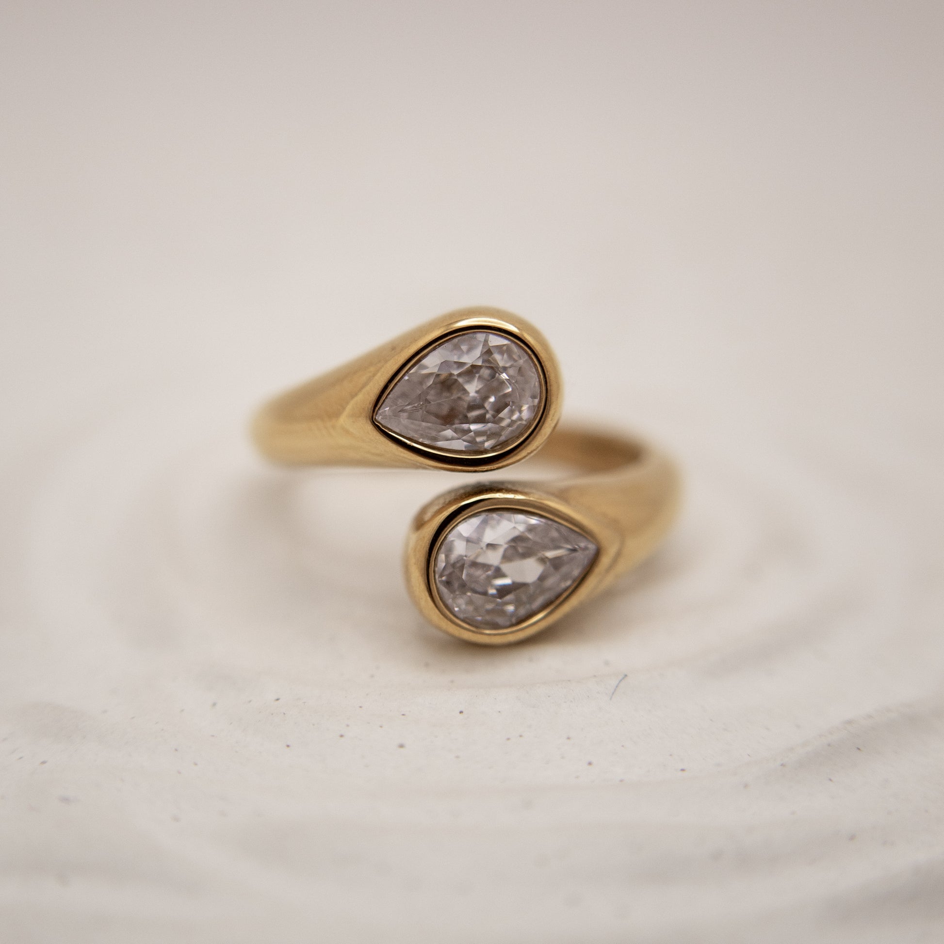 Gold ring with two pear-shaped diamond stones on a light background