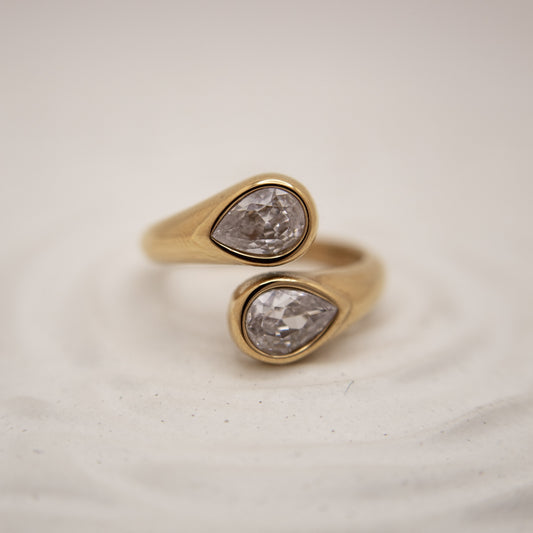 Gold ring with two pear-shaped diamond stones on a light background