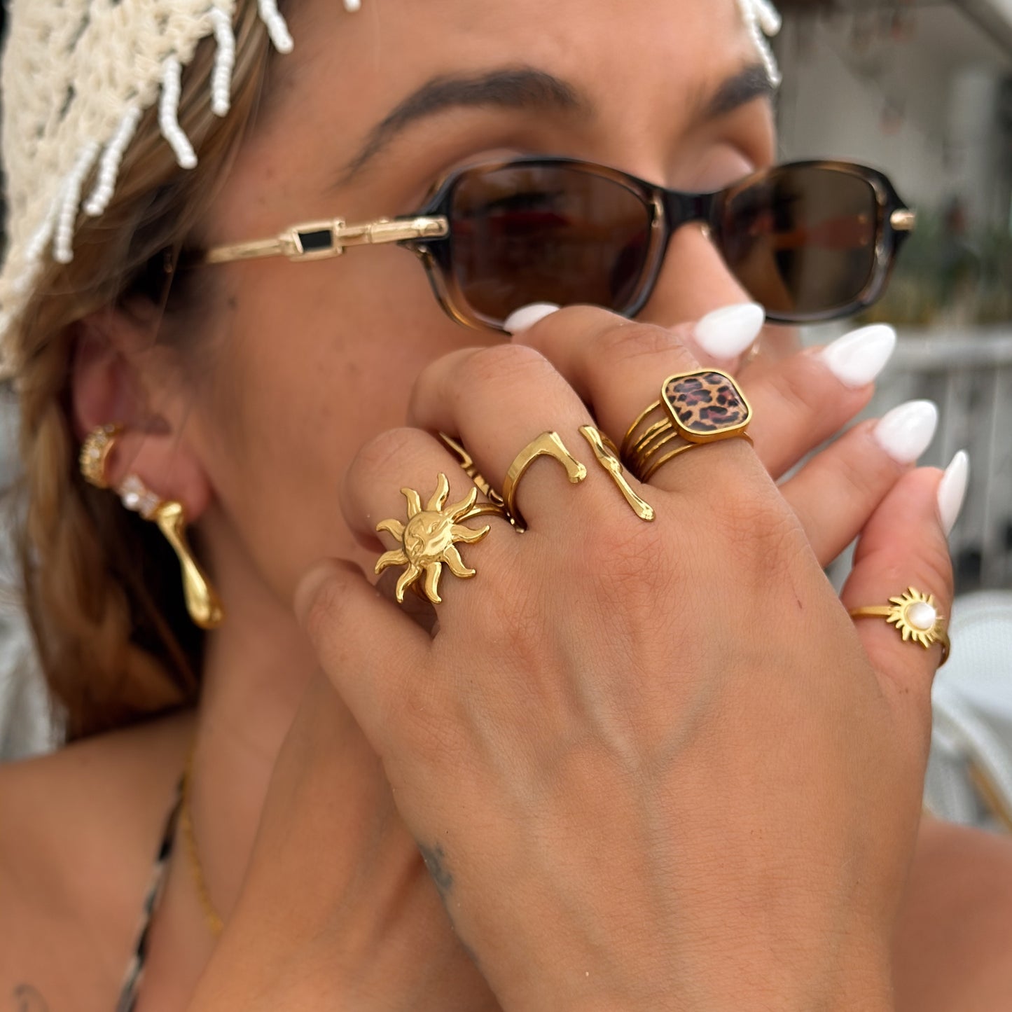 Close-up of a person wearing gold rings and sunglasses with a blurred background