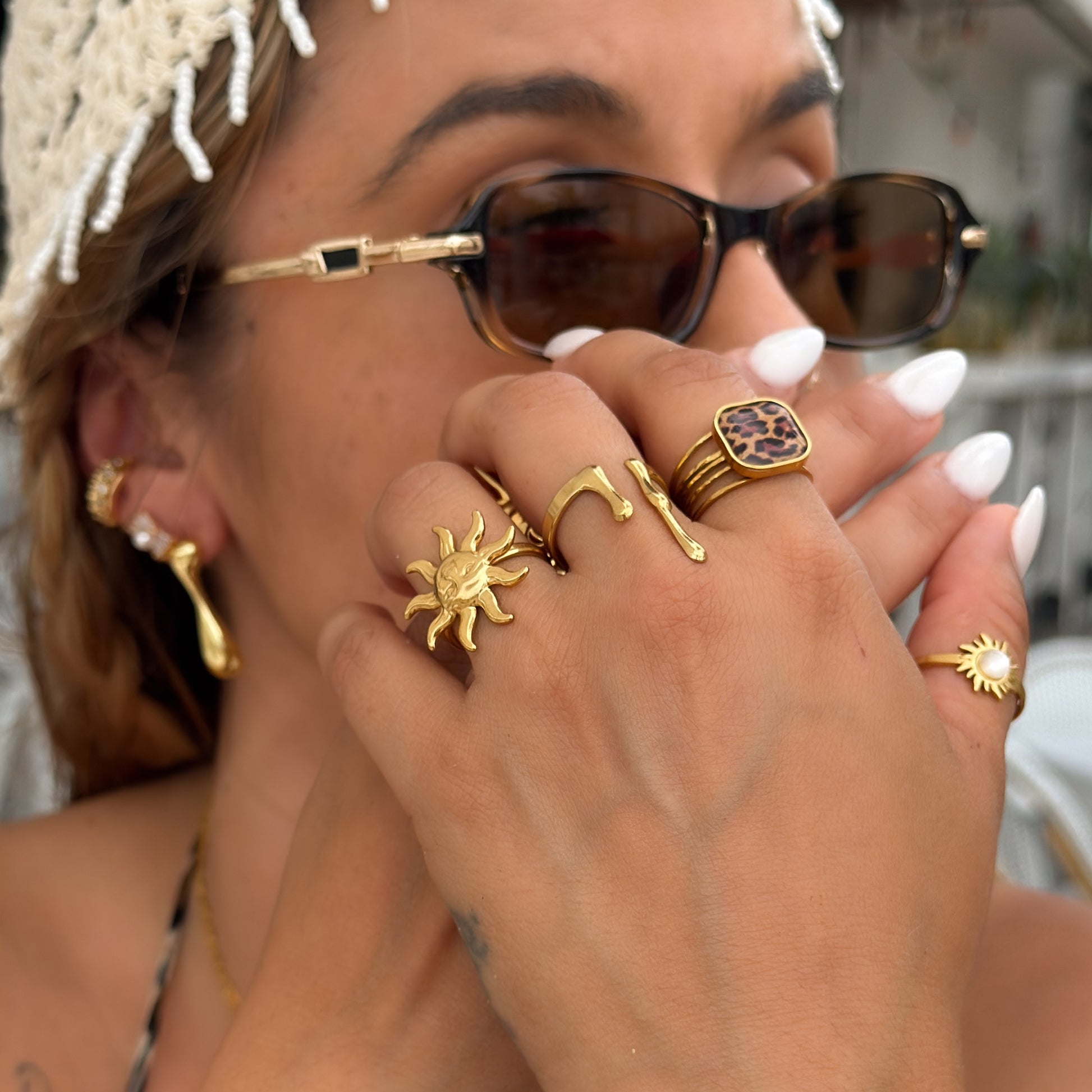Close-up of a person wearing gold rings and sunglasses with a blurred background
