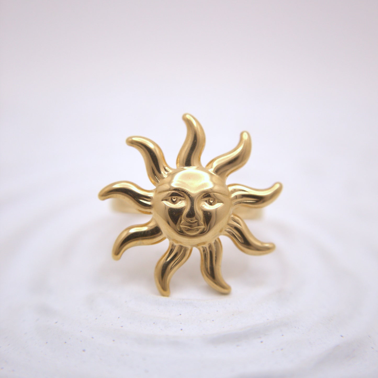Gold sun-shaped brooch with face design on a white background