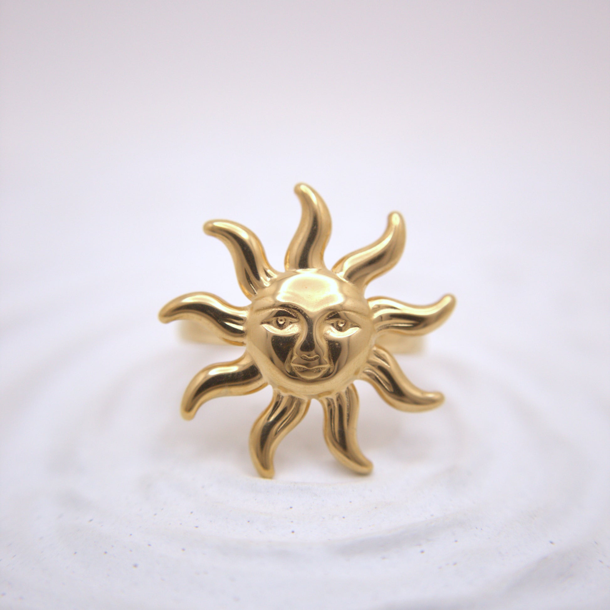Gold sun-shaped brooch with face design on a white background