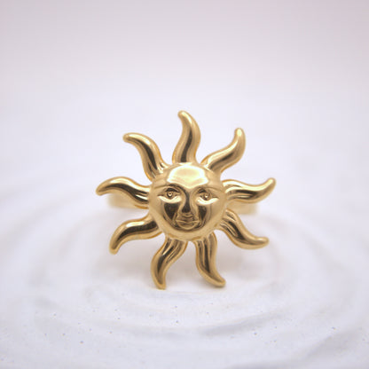 Gold sun-shaped brooch with face design on a white background
