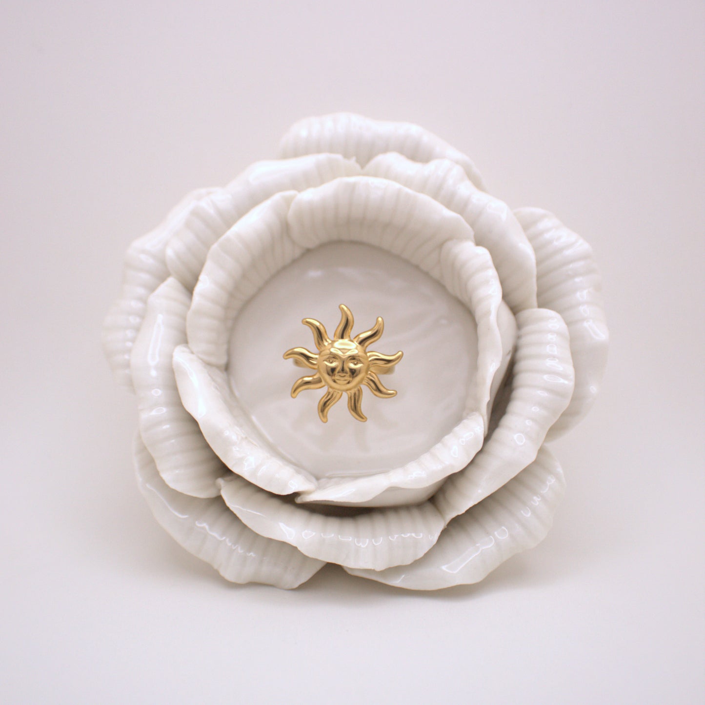 White ceramic flower with a gold sun emblem on a light gray background
