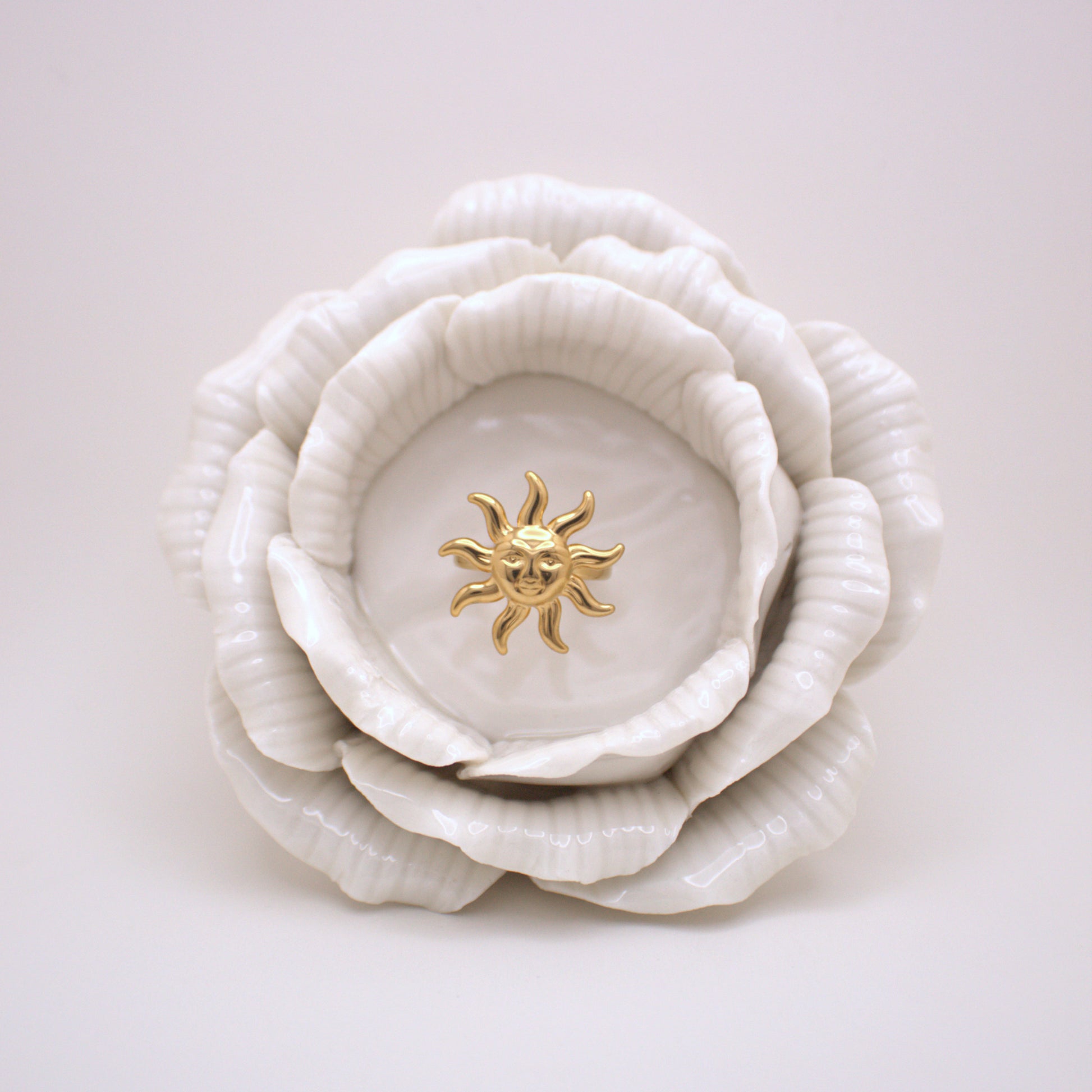 White ceramic flower with a gold sun emblem on a light gray background